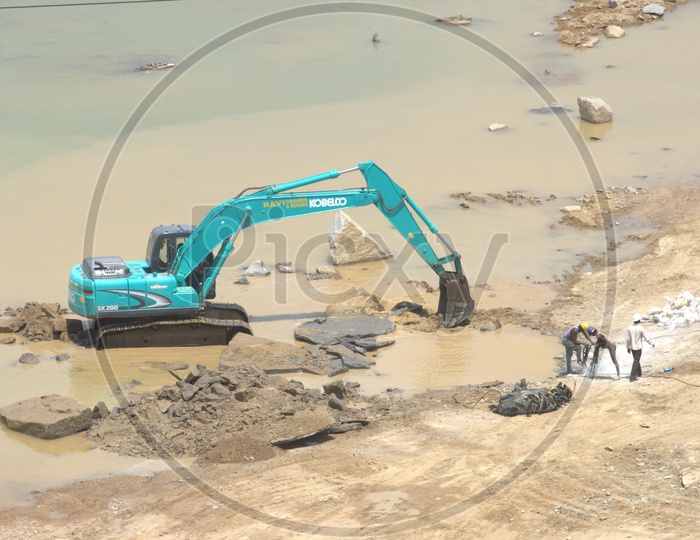 Bulldozer excavating the rock bodies alongside the labourers drilling at a construction site