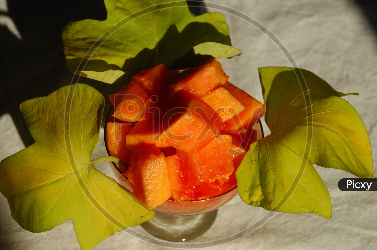 Papaya fruit pieces served in a glass cup with green leaf in the background