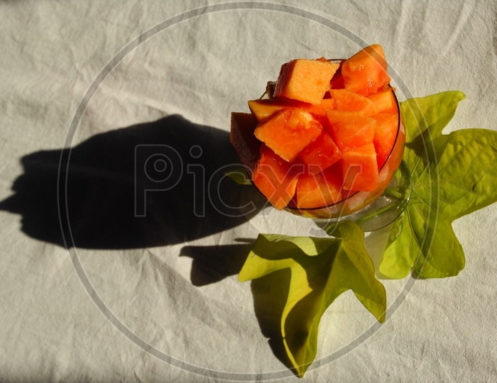 Papaya fruit pieces served in a glass cup with green leaf in the background
