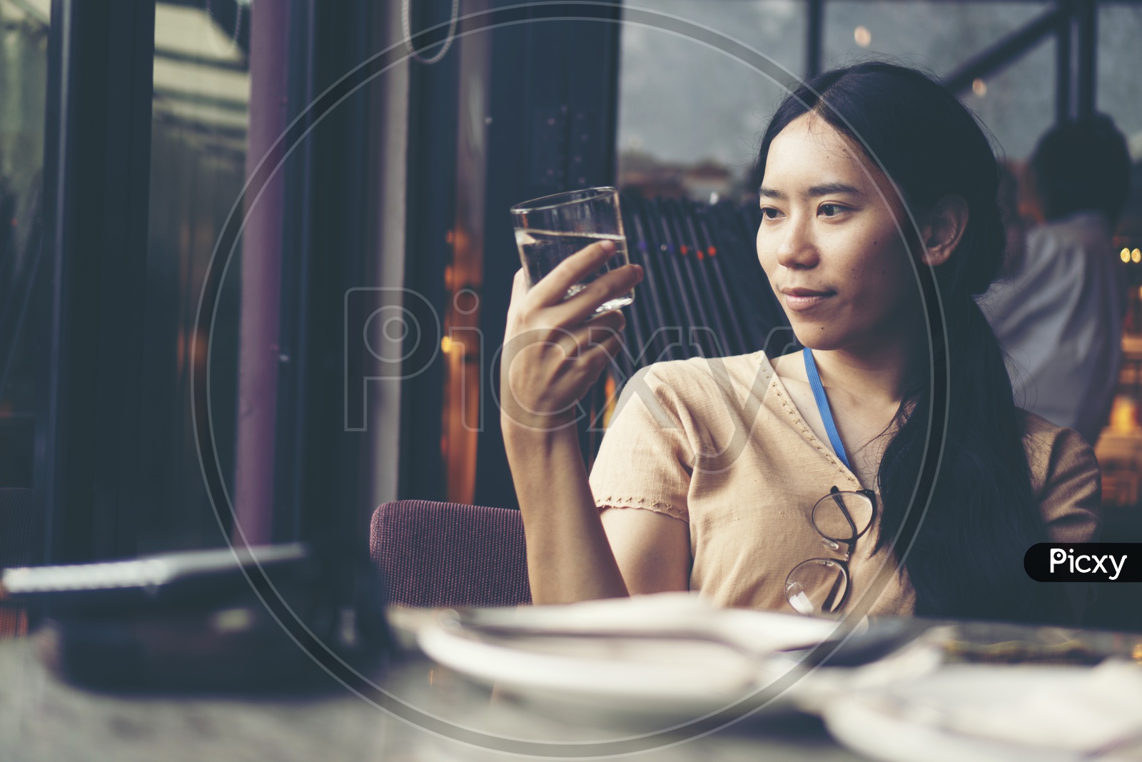 Asian Woman In A Cafe Holding a Water Glass With Smile On Face
