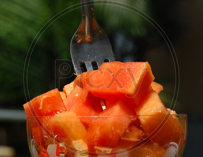 Papaya fruit pieces in a glass cup with fork