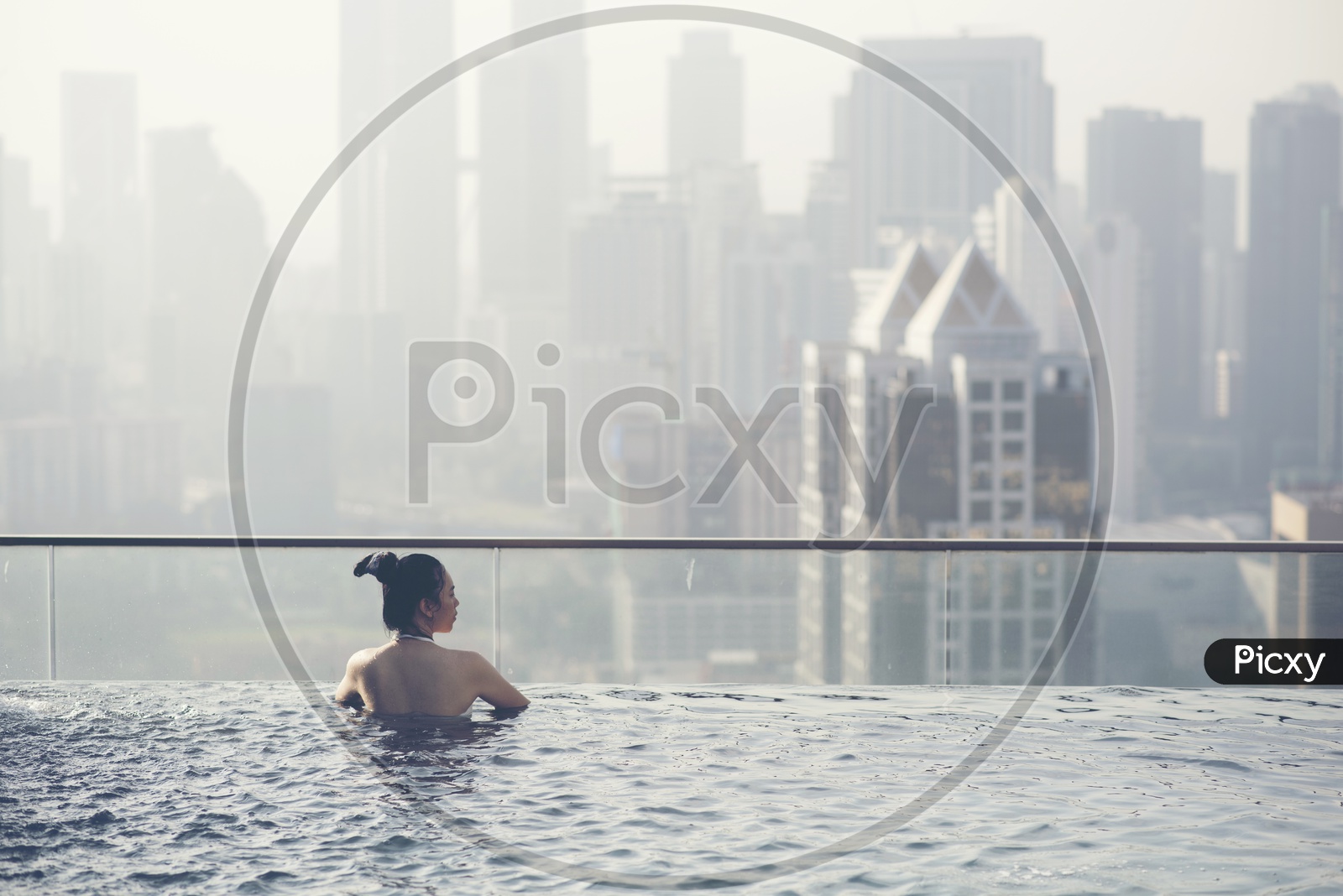 An Asian Woman On a Swimming pool  On a Roof Top Of a High Rise Building With a City View Of Kuala Lumpur