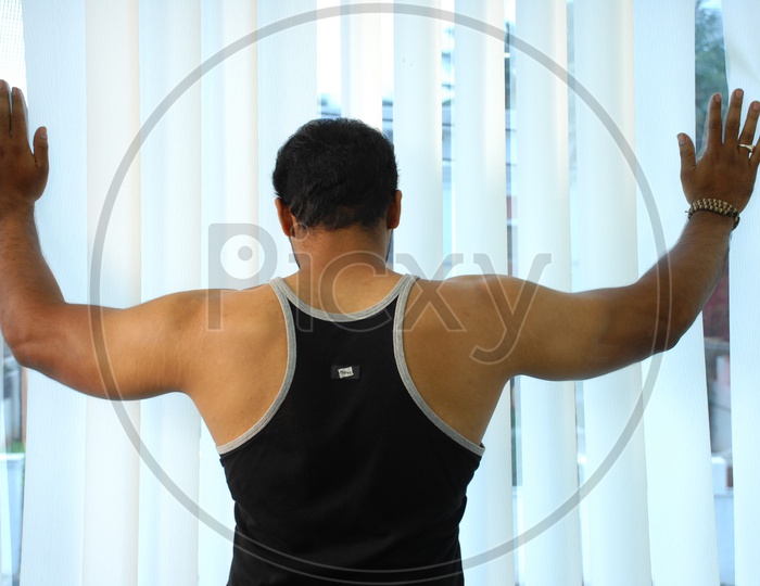 A muscled man showing his back wearing black vest in a Gym