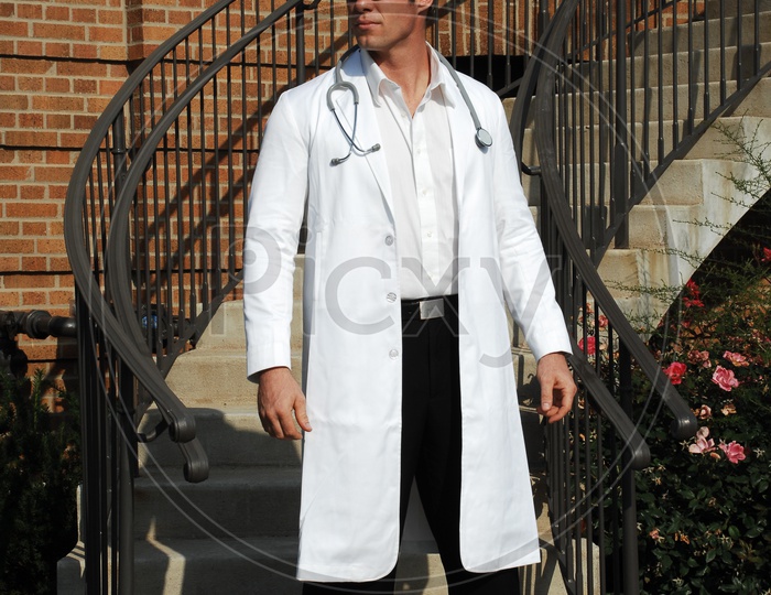 A male doctors wearing white coat with stethoscope at the staircase