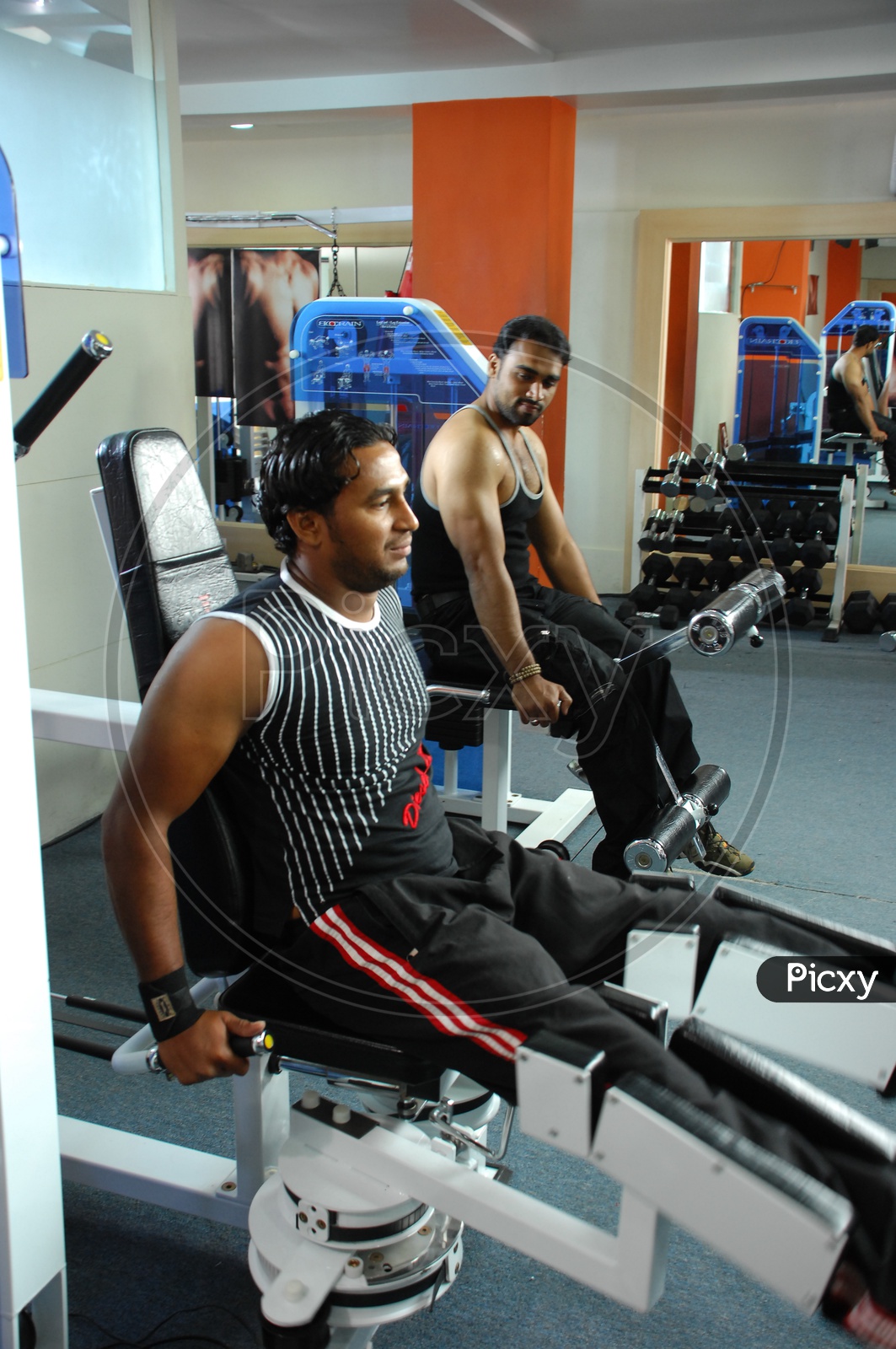 Man doing Leg Adduction / Abduction Machine exercise alongside the man doing leg extension machine in a Gym