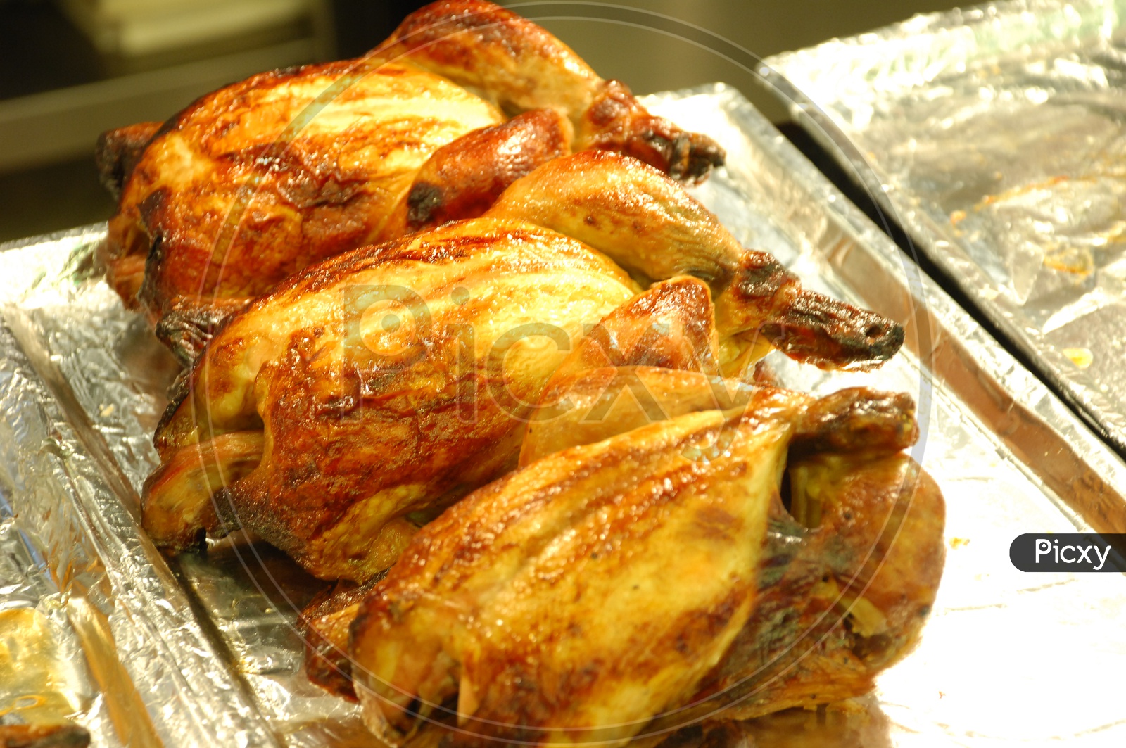 Close up shot of a roasted chicken placed in aluminum foil lined tray