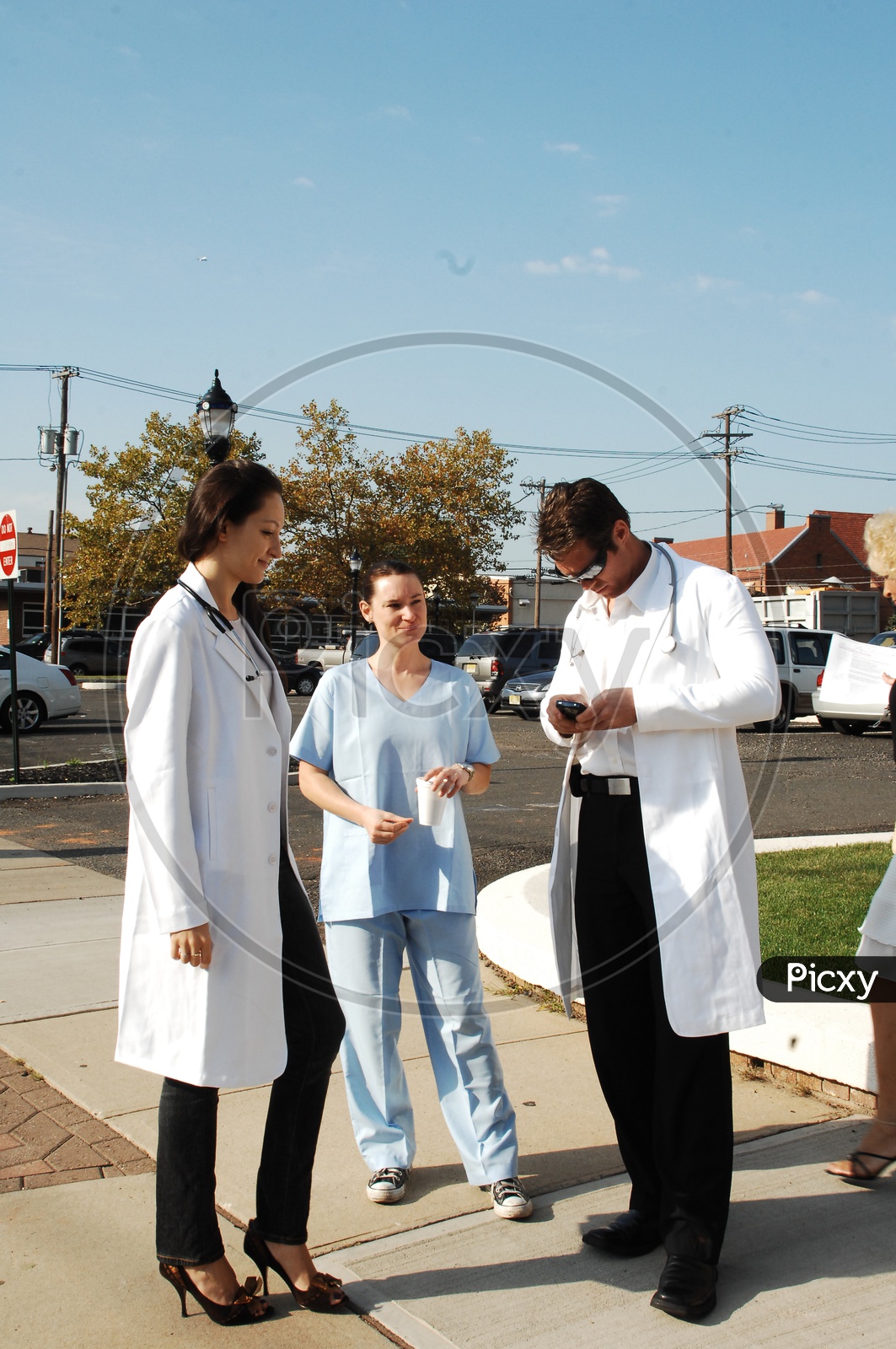 A male and a female doctors wearing white coat with stethoscopes talking to a patient on the road