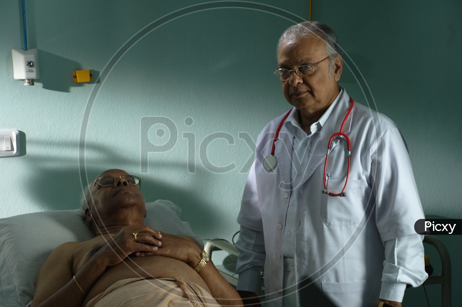 An old male doctor with stethoscope wearing a white coat checking a patient