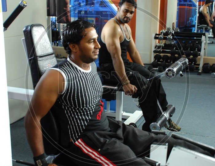 Man doing Leg Adduction / Abduction Machine exercise alongside the man doing leg extension machine in a Gym