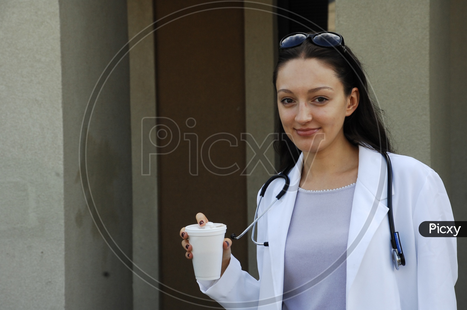 A female doctor wearing white coat with stethoscope and coffee mug