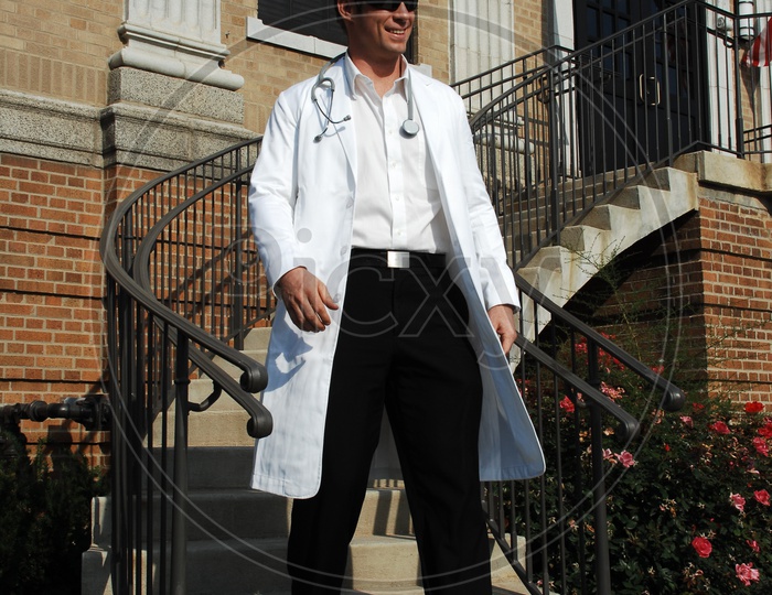 A male doctor wearing white coat with stethoscope waiting down the stairs