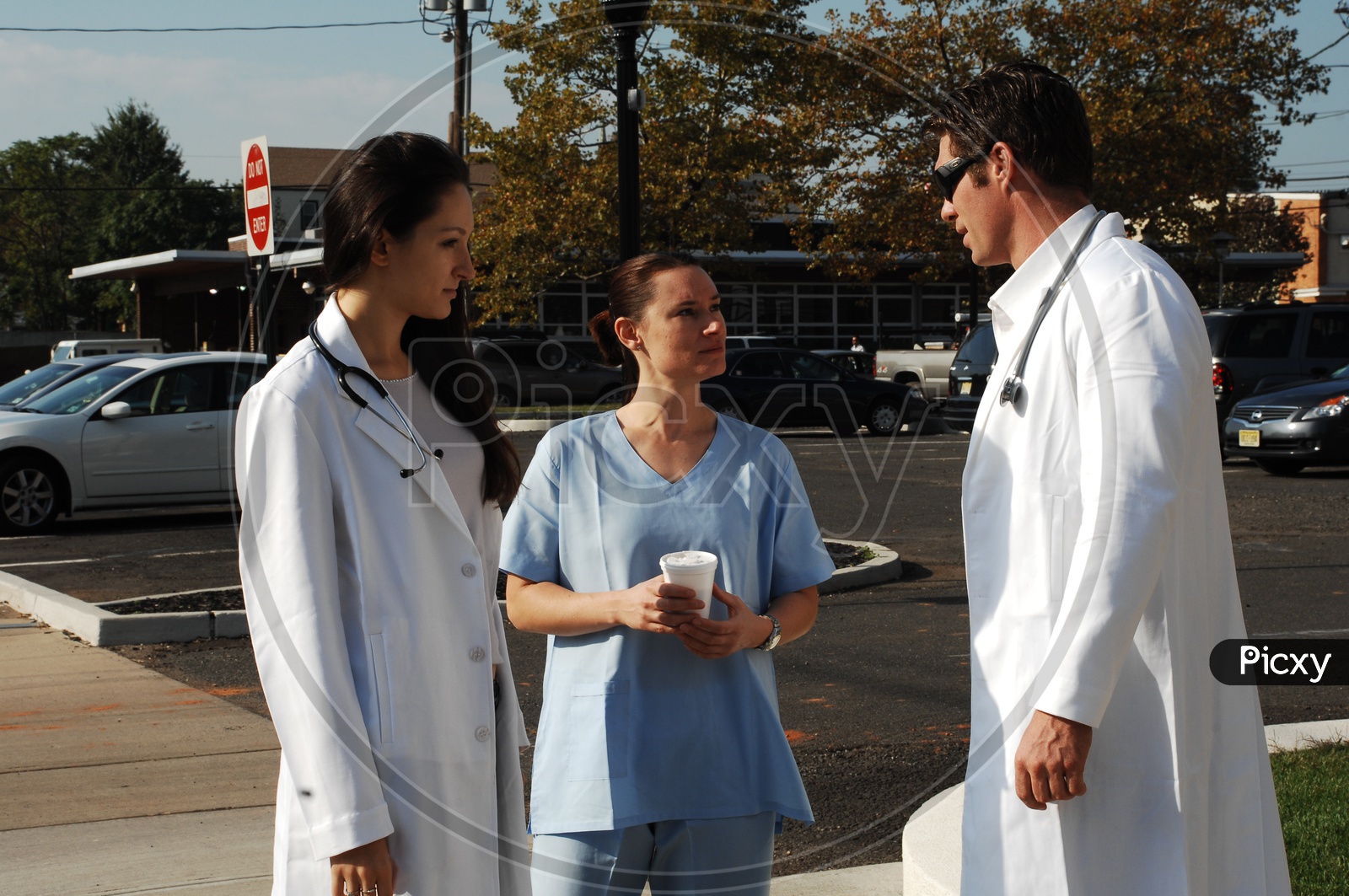 A male and a female doctors wearing white coat with stethoscopes talking to a patient on the road