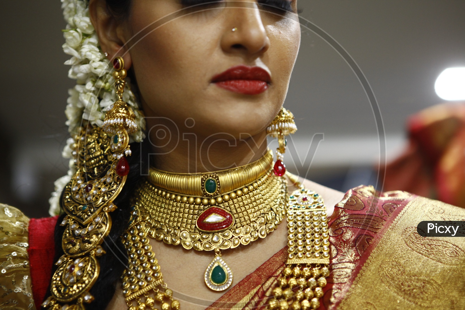 A woman wearing gold choker necklace with Emerald, pearls along with Earrings
