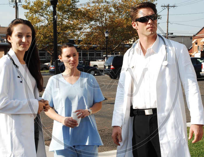 A male and a female doctors wearing white coat with stethoscopes and a patient on the road