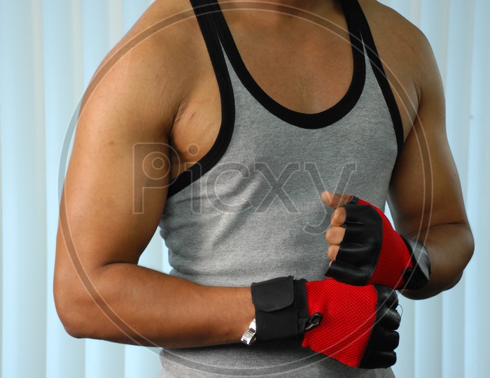 A muscled man wearing grey vest and Red grips in a Gym
