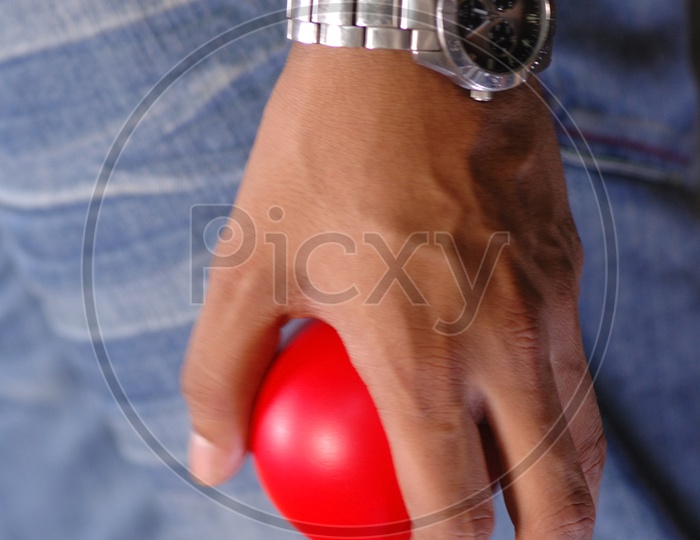 Hand of a man with a steel watch holding a red smiley ball
