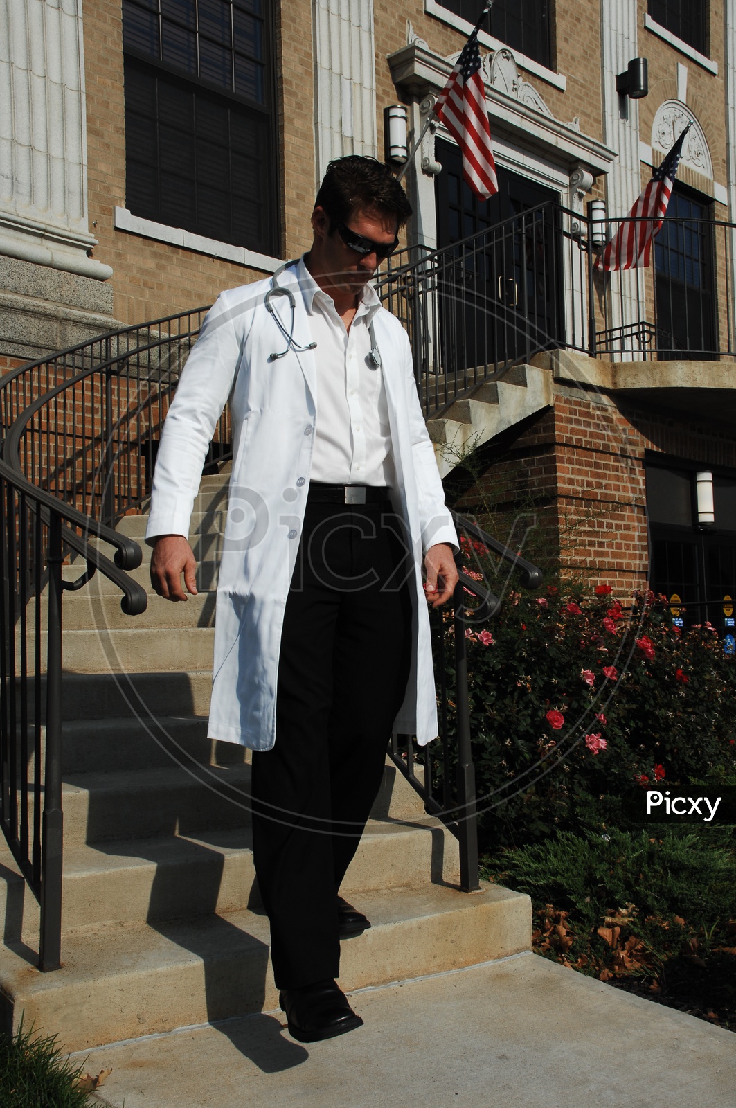 A male doctor wearing white coat with stethoscope walking down the staircase