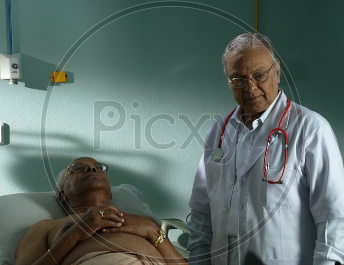 An old male doctor with stethoscope wearing a white coat checking a patient