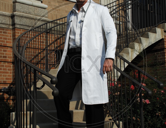 A male doctor wearing white coat with stethoscope walking down the staircase