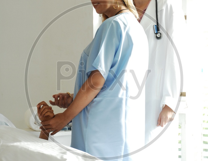 A nurse checking the patient while the doctors stand aside - Movie scene