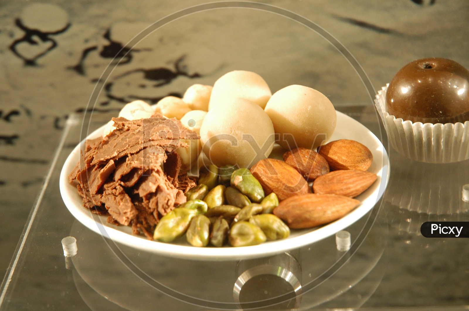 Dry fruits and laddoos in a white plate on a glass table