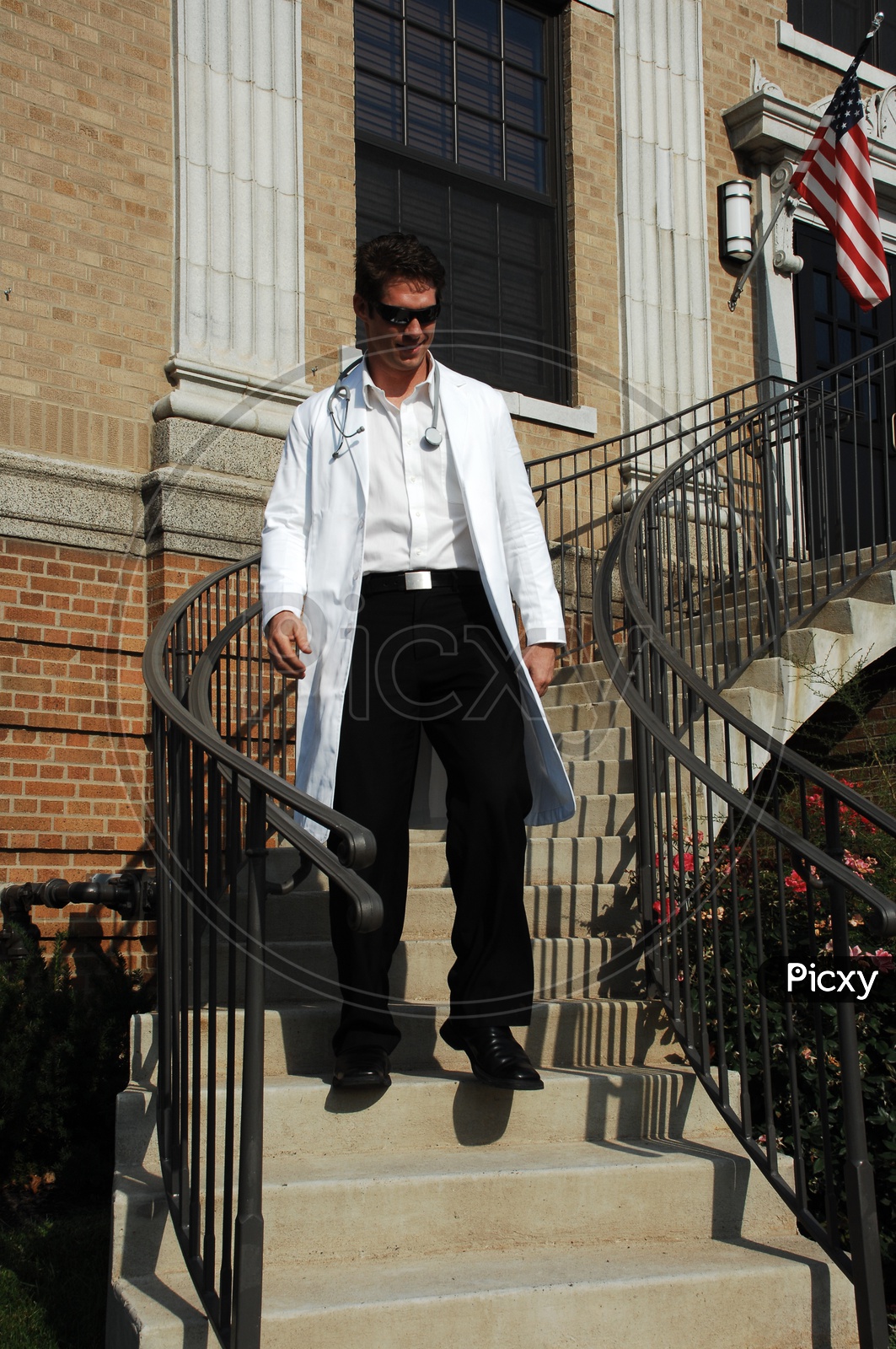 A male doctor wearing white coat with stethoscope waiting down the stairs