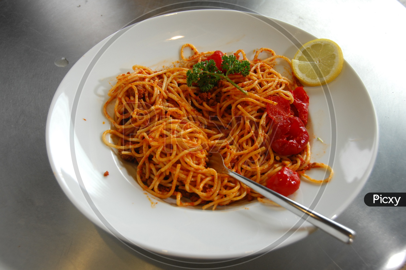 Spicy noodles topped with cherry tomatoes, parsley and a lemon slice served in a white bowl