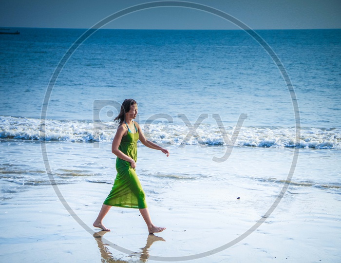 A Lady Walking Along A Beach With Beach Waves And  Blue Sea in Background