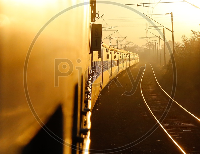 Moving Train  With Luminous Golden Sunlight On it With track and Electricity Poles