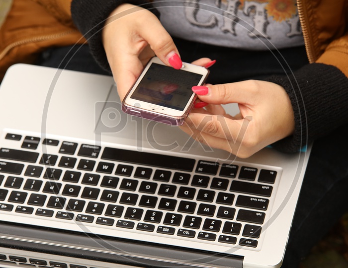 A mobile phone in the hands and a laptop