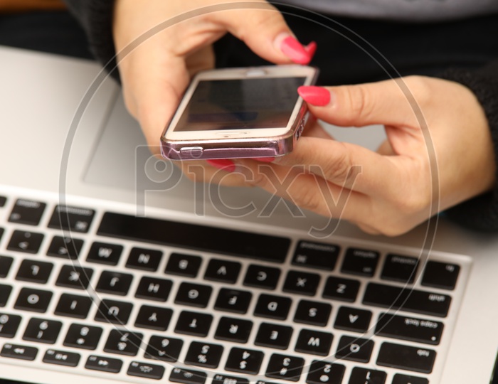A mobile phone in the hands and a laptop