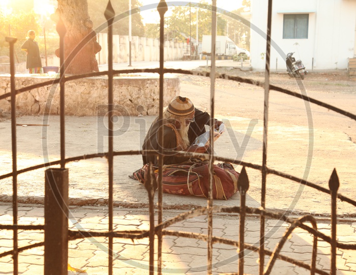 An old man sitting on a road along with his bag and reading a paper in Varanasi