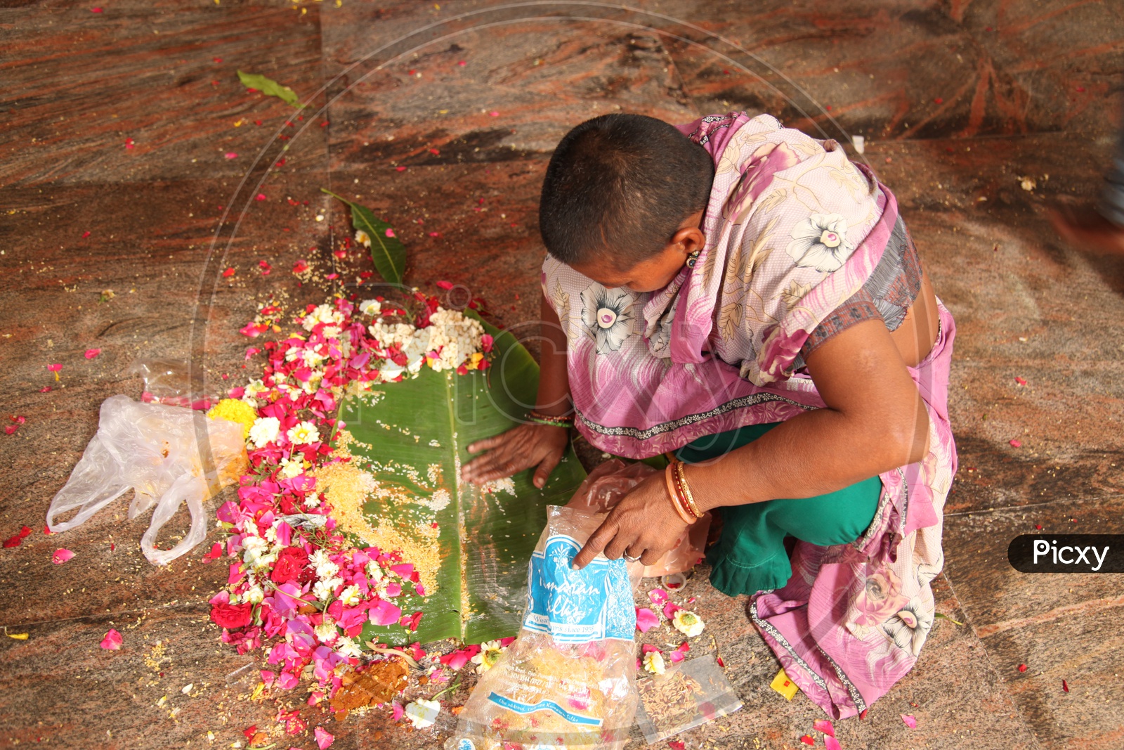 A woman devotee collecting the flowers and other puja items into a plastic cover from a plantain leaf