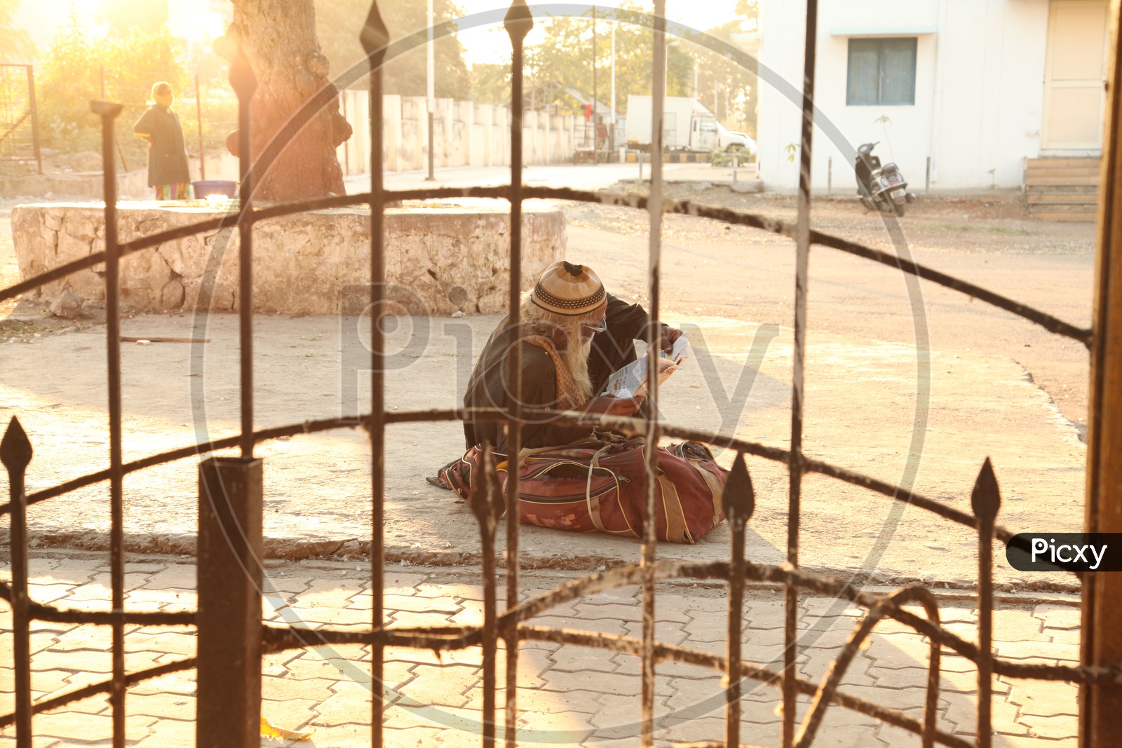 An old man sitting on a road along with his bag and reading a paper in Varanasi