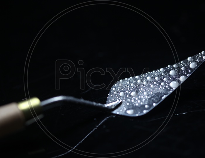 Water Droplets On a Spatula Over a Dark Black Background