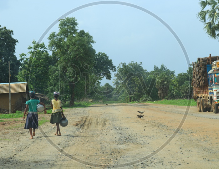 Girls carrying water cans on a road