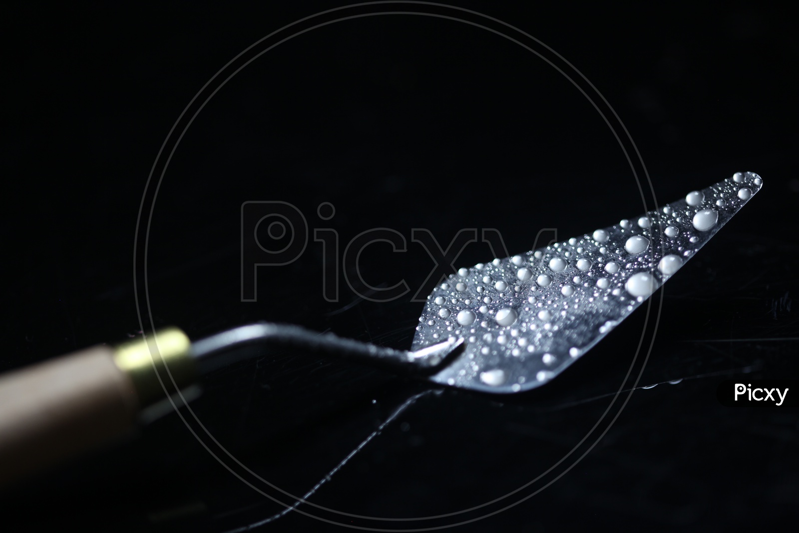 Water Droplets On a Spatula Over a Dark Black Background