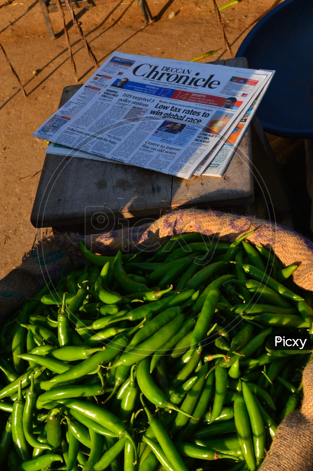 Green chillies in a gunny bag and newspaper on a wooden chair