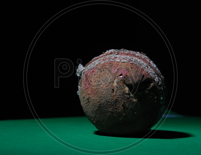 A used and worn out cricket ball in green and black background