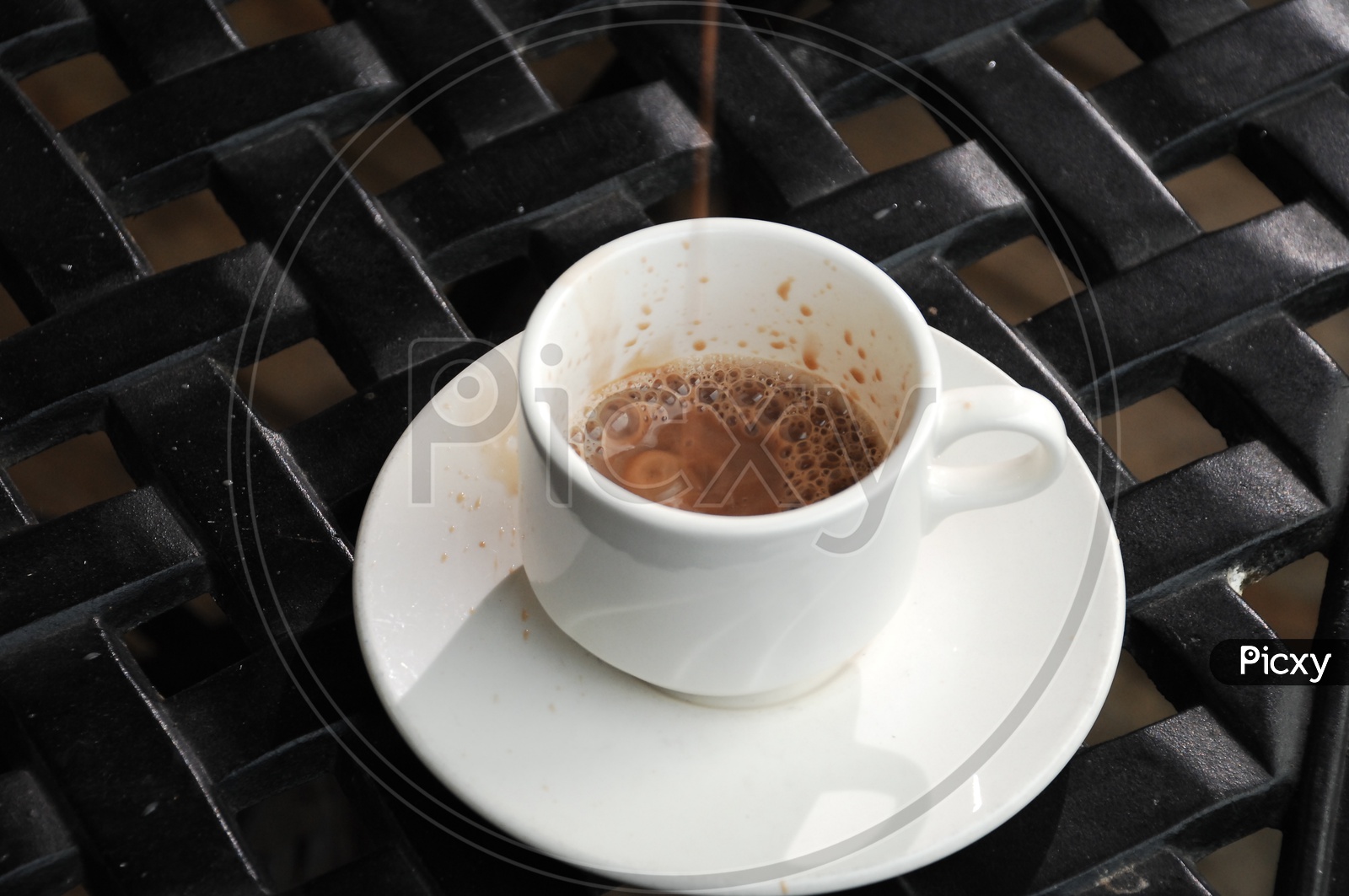 A white cup of black tea on a saucer with a black background