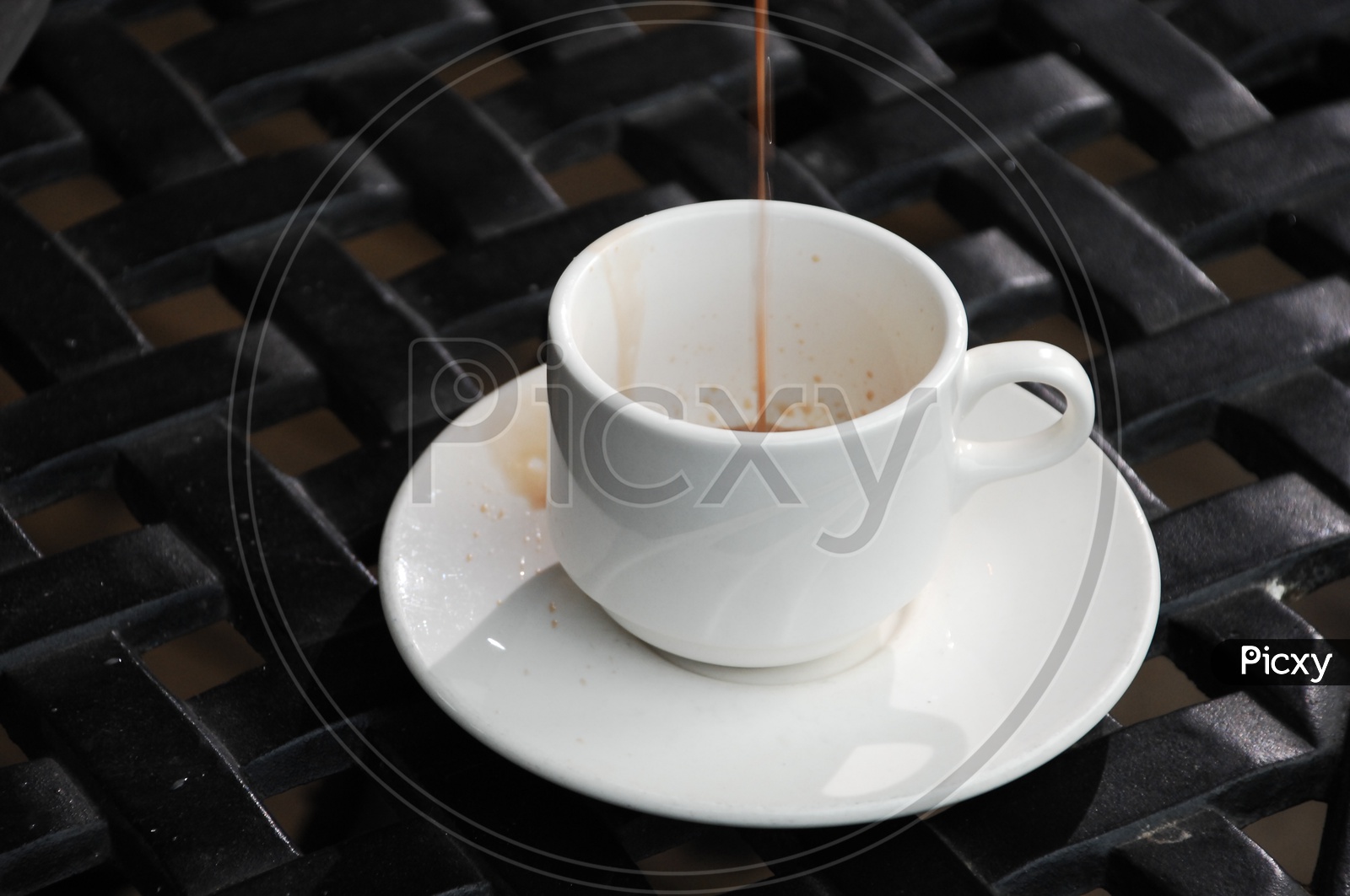 A white cup of black tea on a saucer with a black background