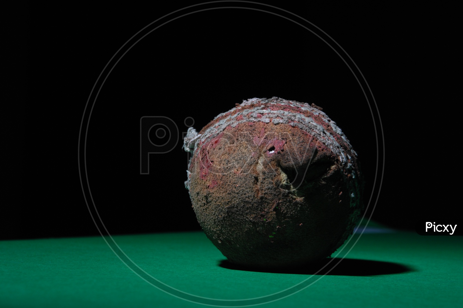 A used and worn out cricket ball in green and black background
