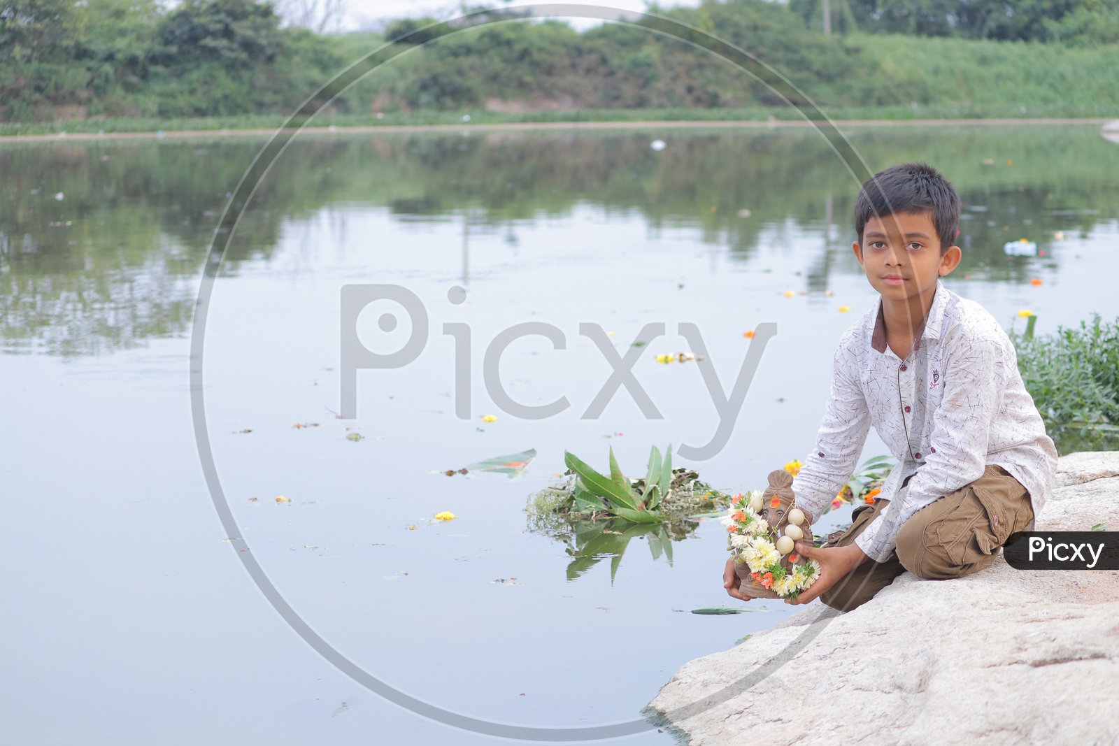 A child holding clay Ganesha near a lake