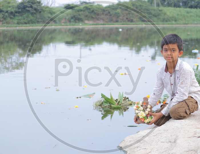 A child holding clay Ganesha near a lake