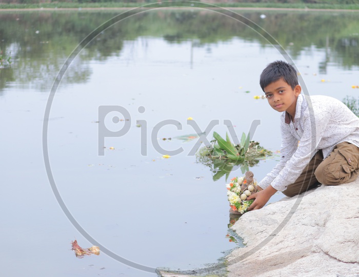 A young boy immersing mud Ganesha in the lake