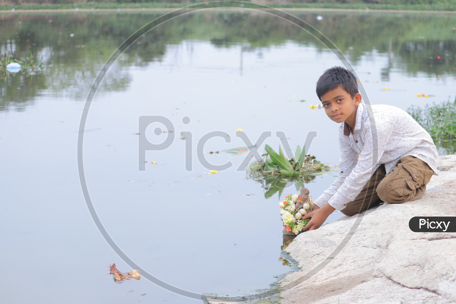 A young boy immersing mud Ganesha in the lake