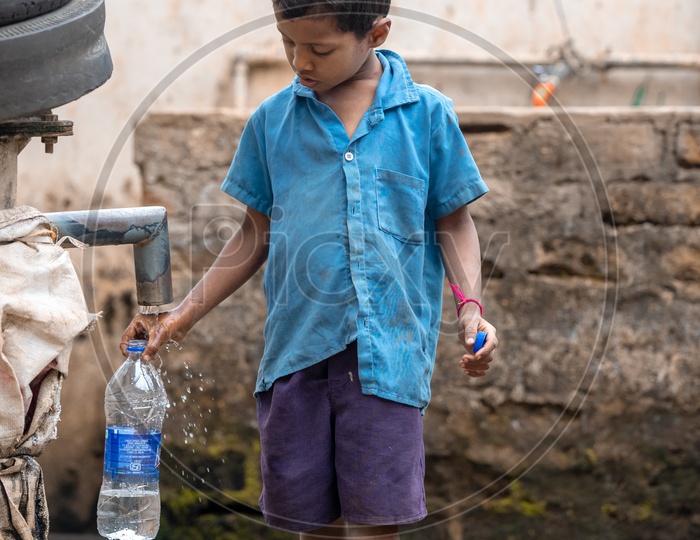A primary school student filling his water bottle near a hand pump