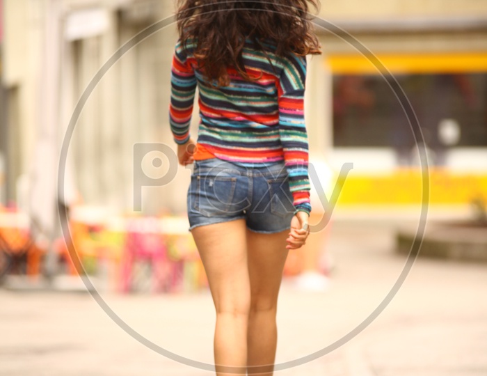 A girl in colorful striped tee and shorts walking on the road