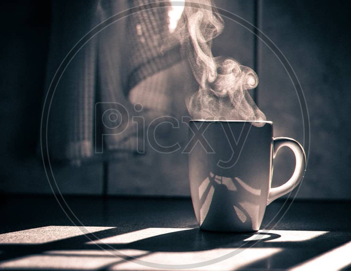 A coffee mug with smoke coming out of it and sunlight in the backdrop