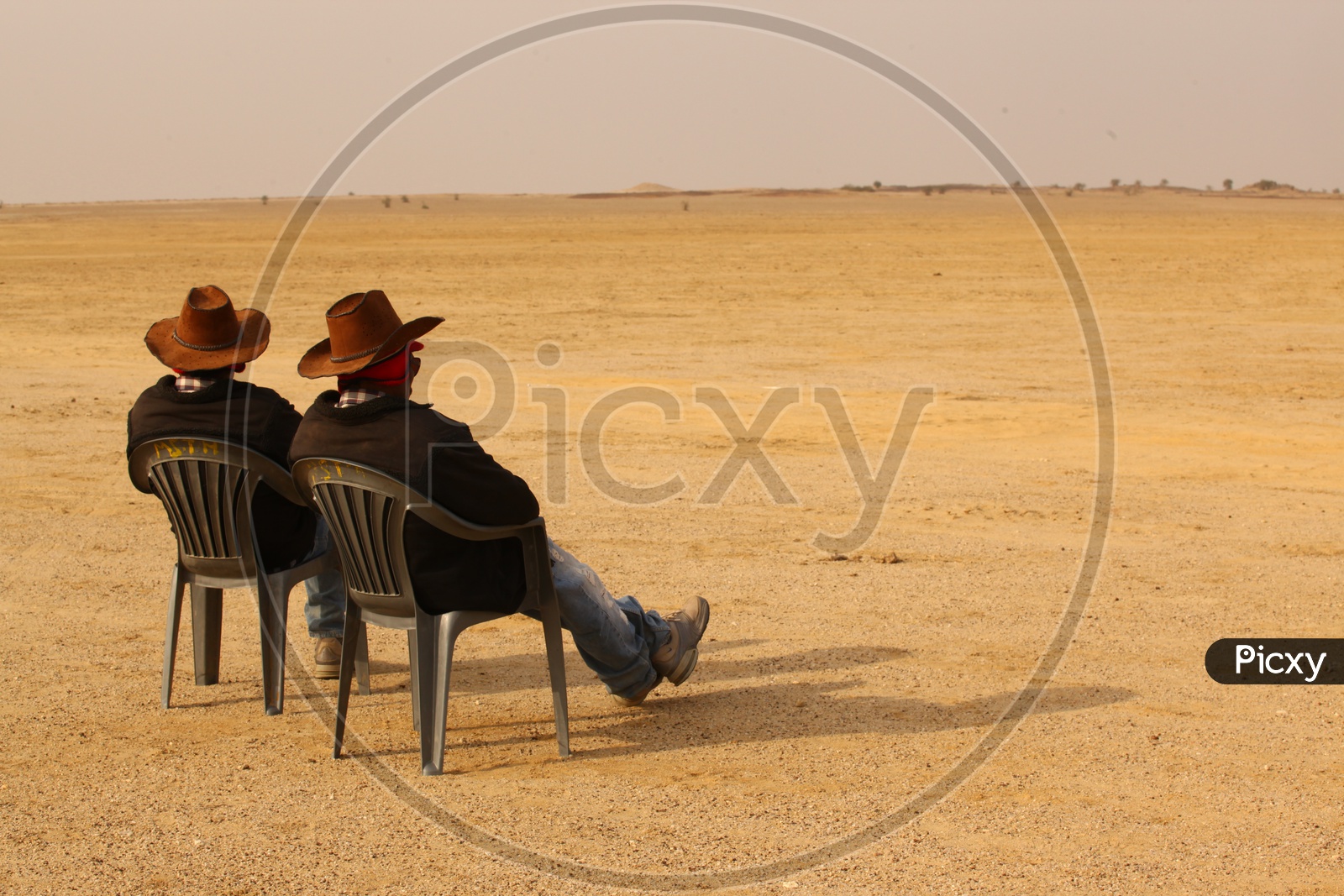 Two men with hats sitting in the chairs at a desert